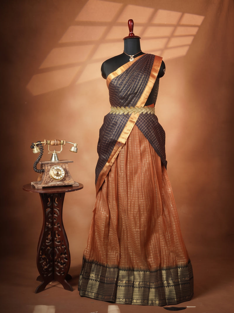 A traditional Indian saree displayed on a black mannequin dress form, styled with a vintage rotary telephone on a carved wooden side table. The saree features a dark charcoal gray body with a shimmering gold border, a gold waist belt, and a warm rust-orange lower drape with a matching gold border.