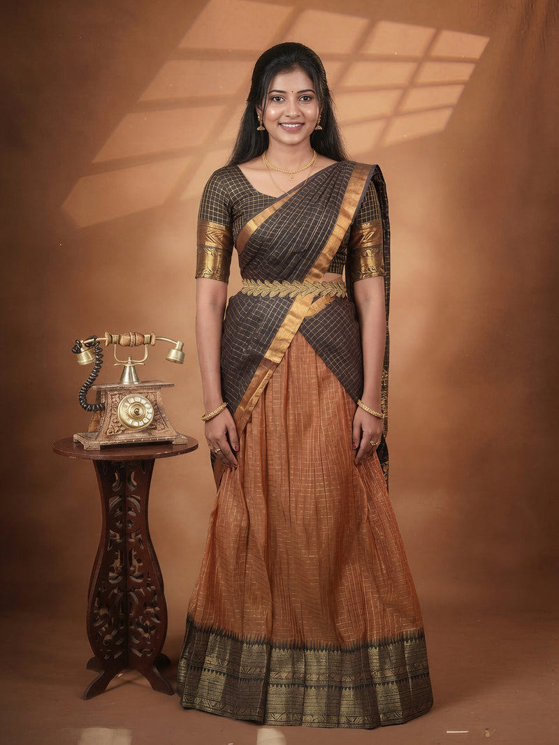 A woman modeling a traditional Indian salwar kameez outfit with a dark gray and gold checkered top and a rust-orange skirt, standing next to a vintage rotary phone on a wooden stand against a warm brown studio backdrop.