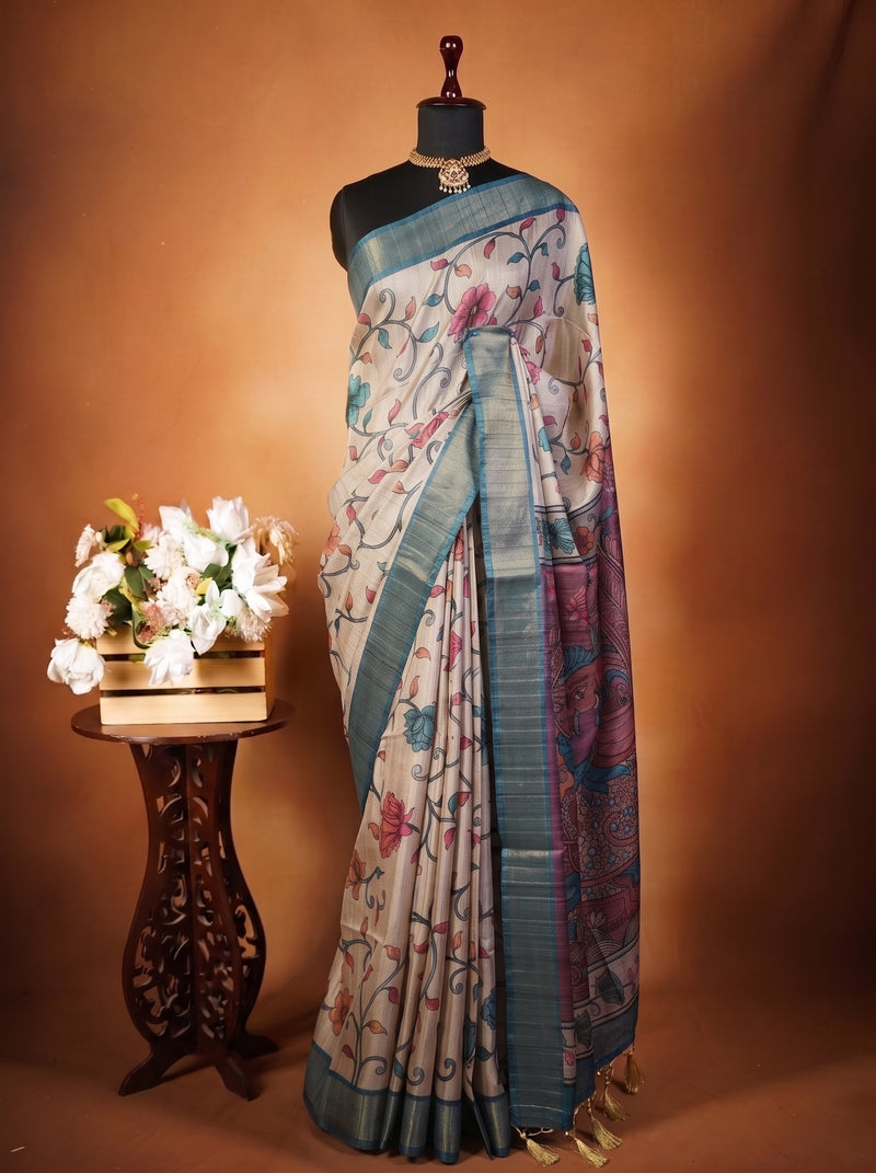 A patterned silk saree draped on a black mannequin torso, styled next to a small wooden table with white flowers against a warm brown studio backdrop.