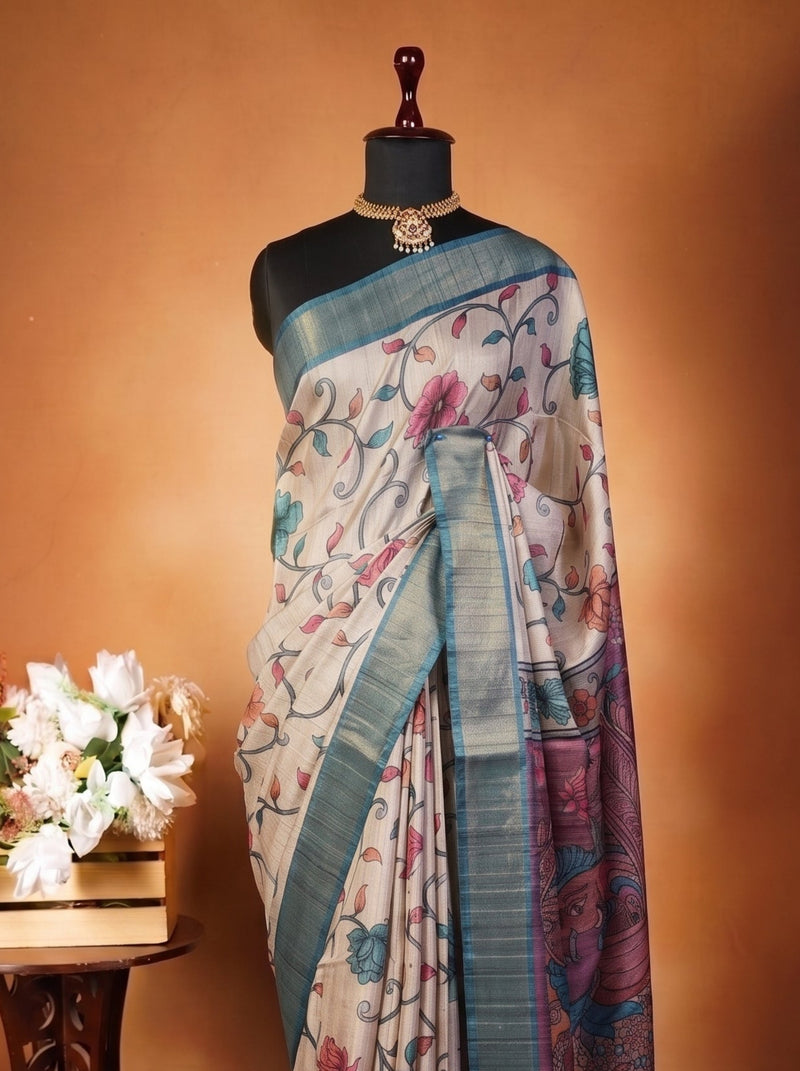 A patterned silk saree draped on a black mannequin torso, styled next to a small wooden table with white flowers against a warm brown studio backdrop.