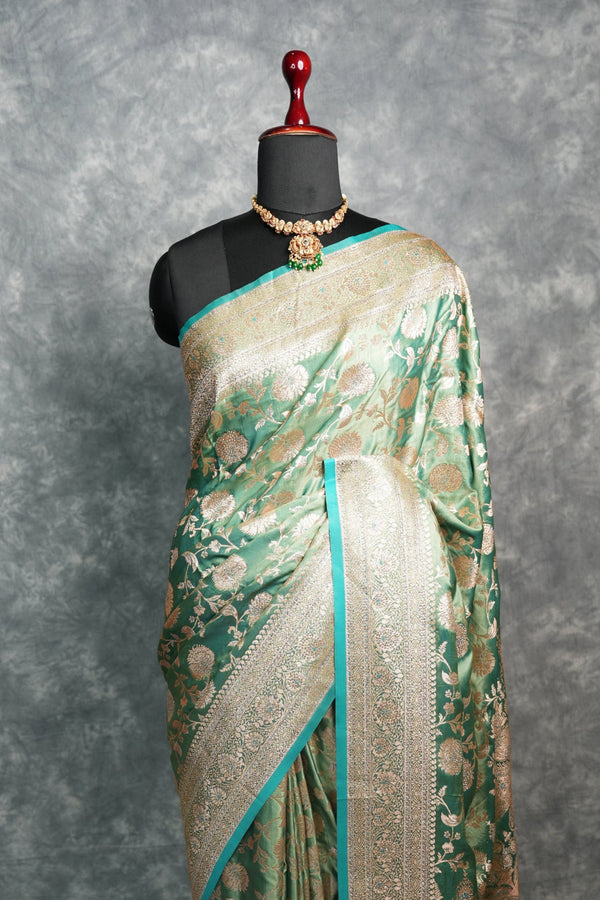 Saree with gold and green patterns on a mannequin against a gray background