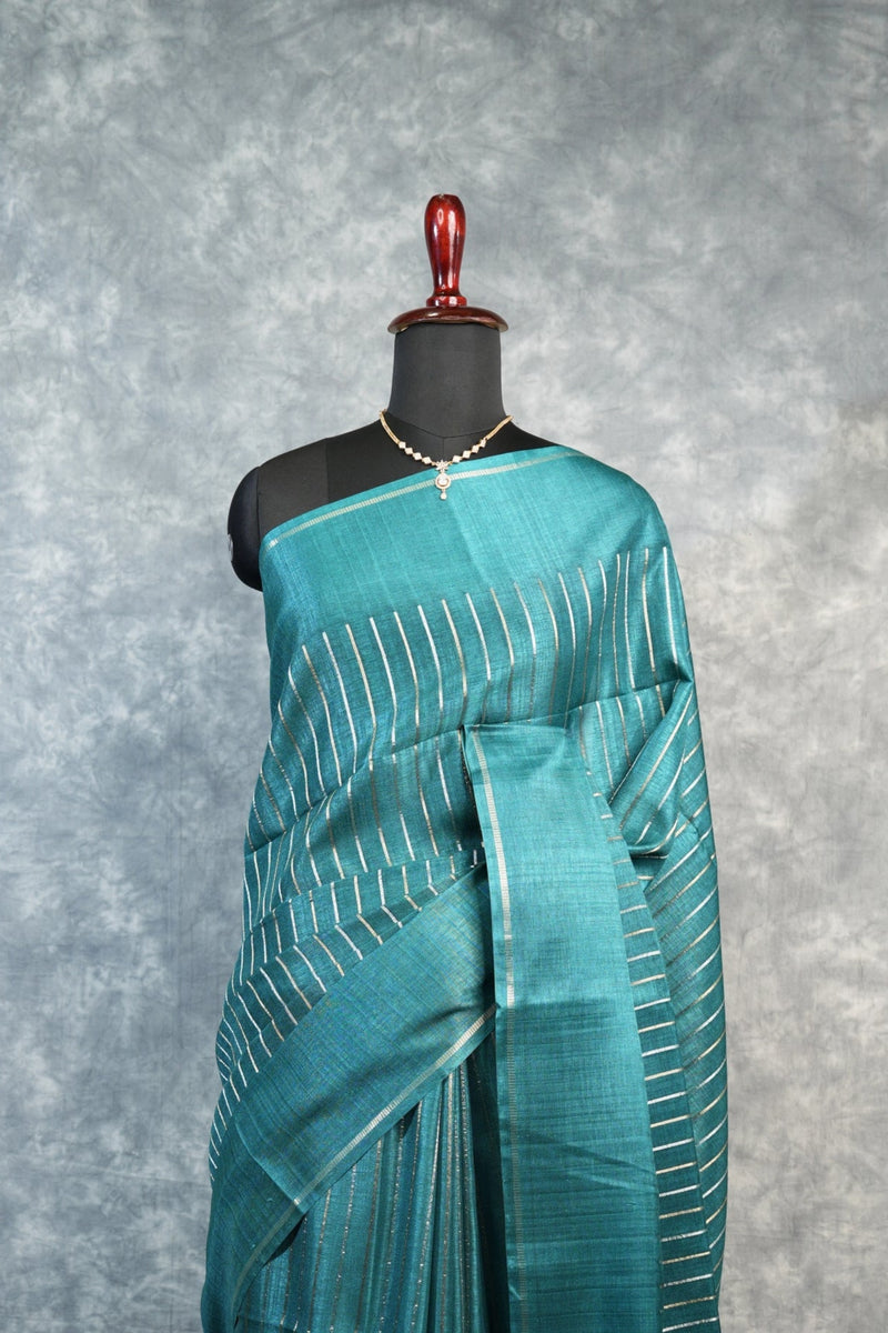 Teal saree with white patterns on a mannequin against a gray background