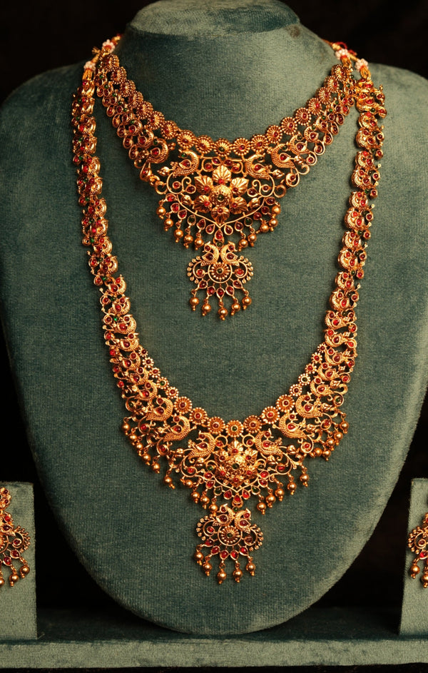 Ornate gold necklace and earrings set on a green velvet stand against a dark background