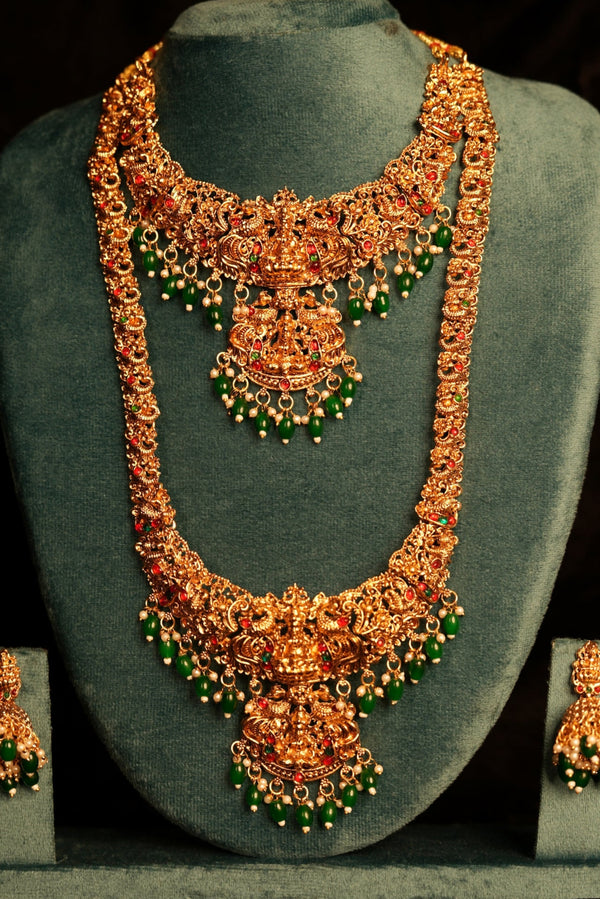 Ornate necklace and earrings set on a gray stand against a black background