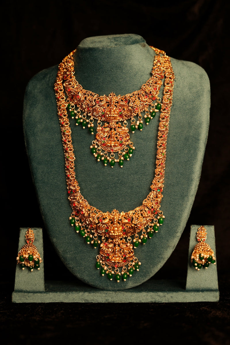 Ornate necklace and earrings set on a gray stand against a black background