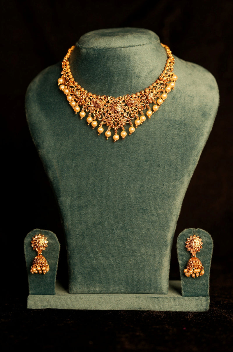 Gold necklace and earrings on a green velvet stand against a black background
