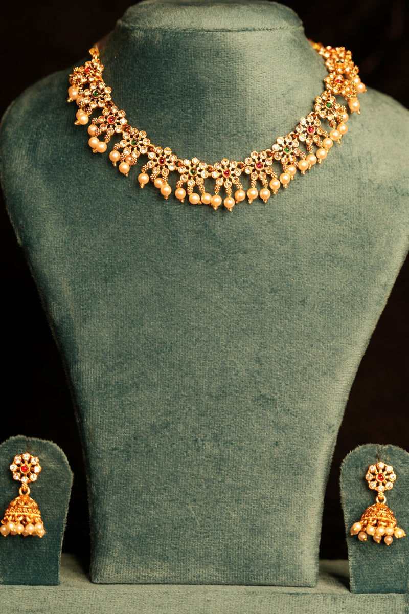Gold necklace and earrings on a green velvet stand against a dark background