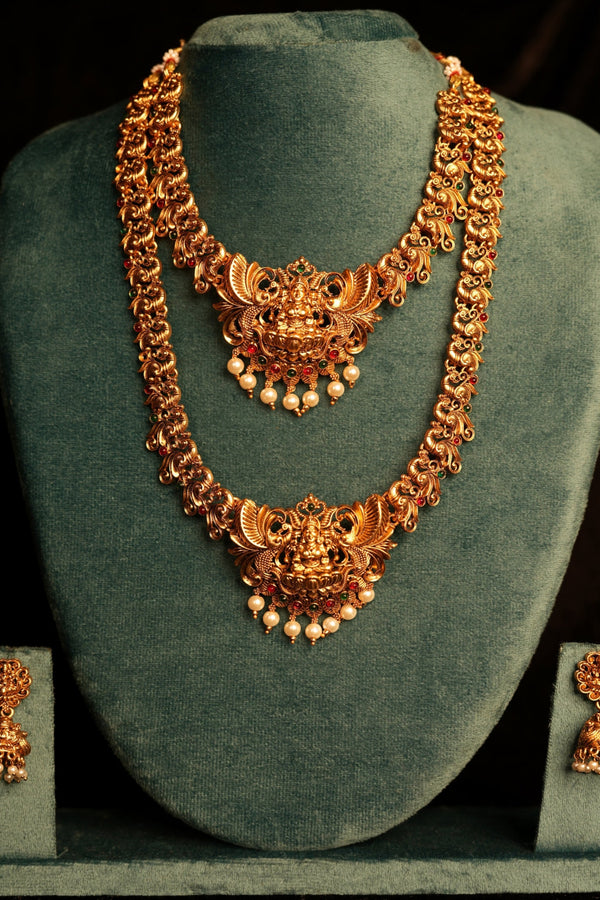 Gold necklace and earrings on a green velvet stand against a dark background