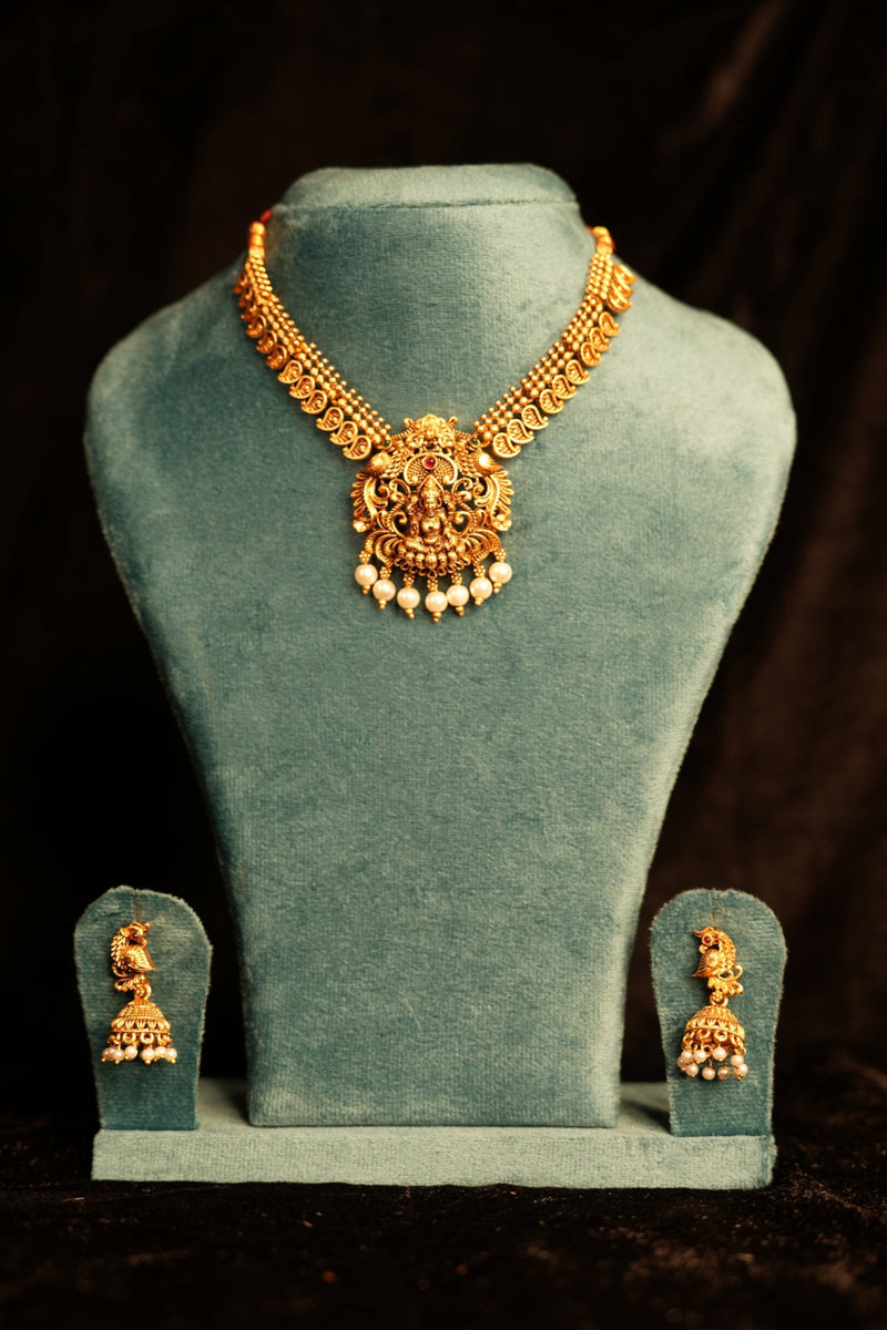 Gold necklace on a green velvet stand against a dark background