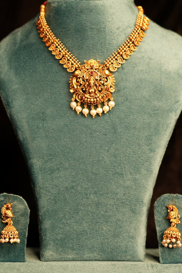 Gold necklace on a green velvet stand against a dark background