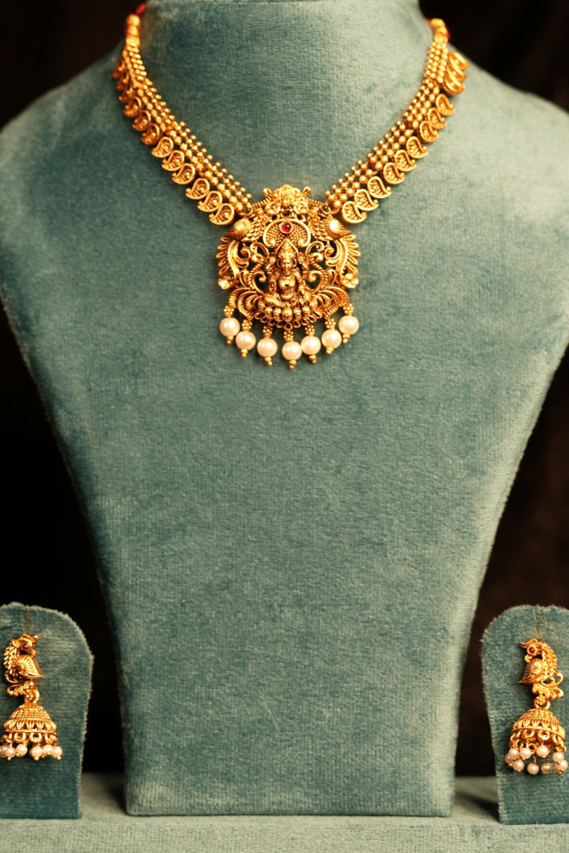 Gold necklace on a green velvet stand against a dark background