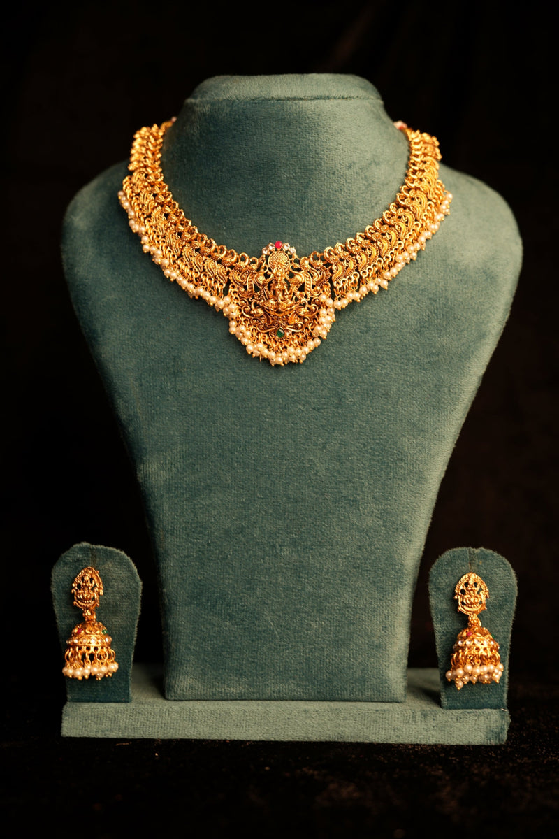 Gold necklace and earrings on a green velvet stand against a dark background
