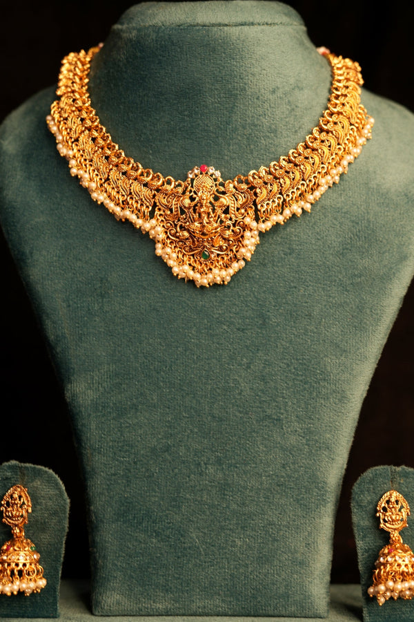 Gold necklace and earrings on a green velvet stand against a dark background
