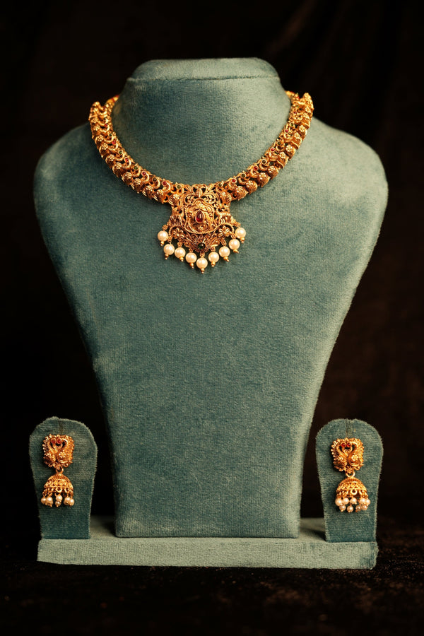 Gold necklace and earrings on a green velvet stand against a dark background