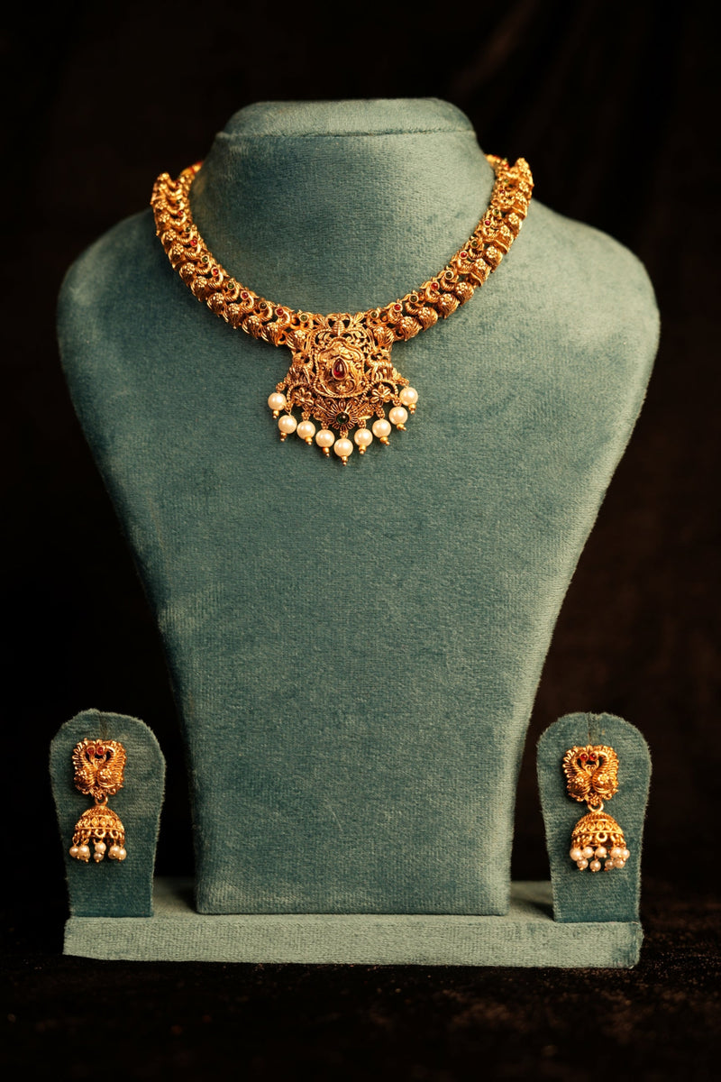 Gold necklace and earrings on a green velvet stand against a dark background