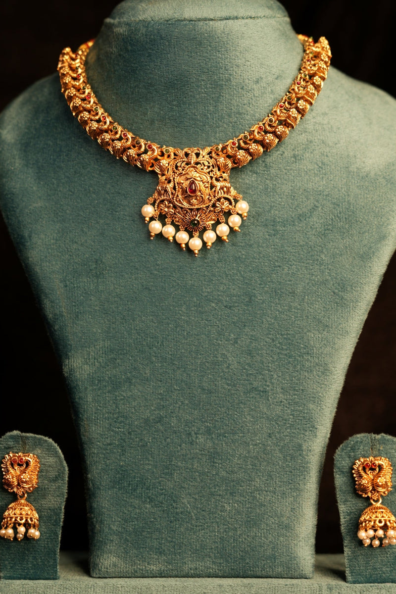 Gold necklace and earrings on a green velvet stand against a dark background