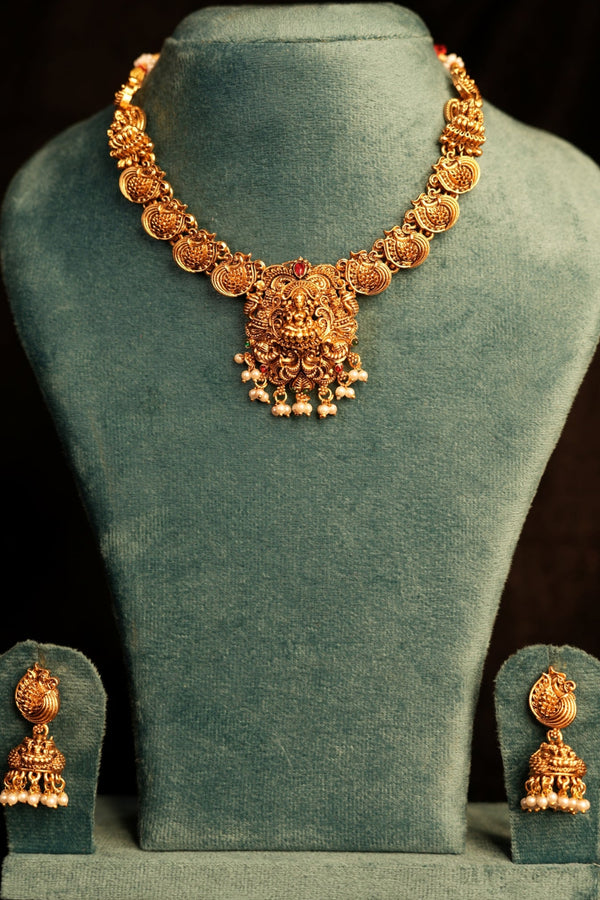 Gold jewelry set on a green velvet stand against a dark background
