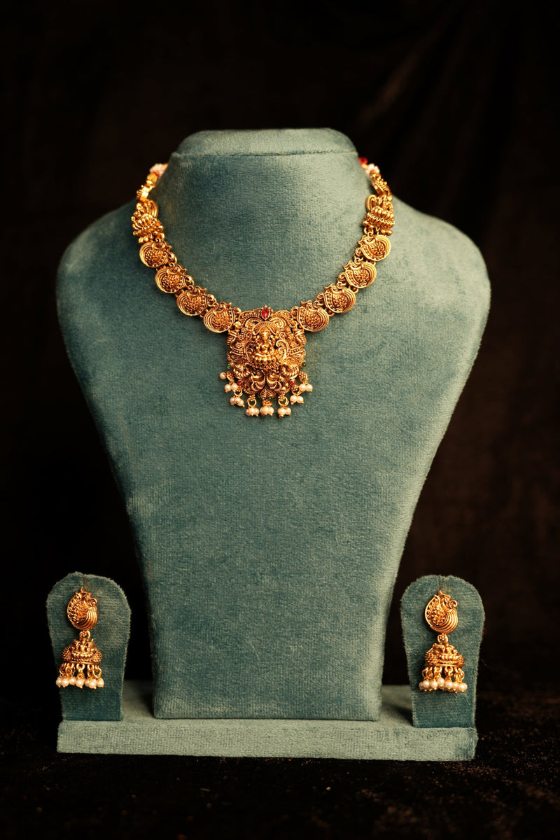 Gold jewelry set on a green velvet stand against a dark background
