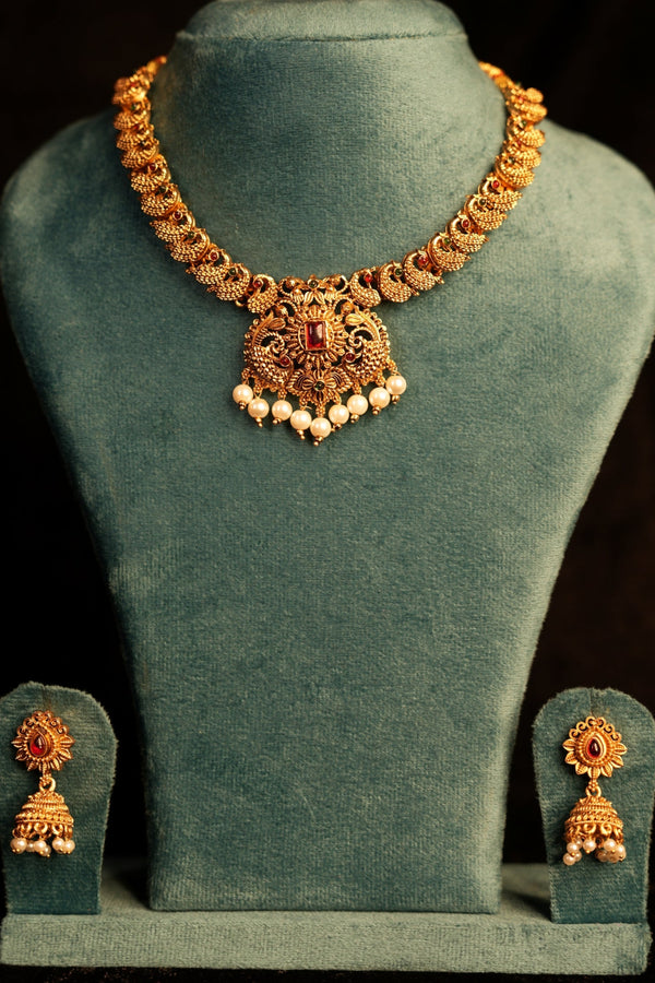 Gold jewelry set including a necklace and earrings on a green velvet stand against a dark background.