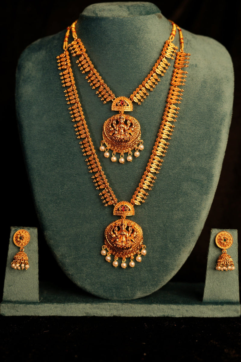 Gold necklace and earrings set on a green velvet stand against a black background