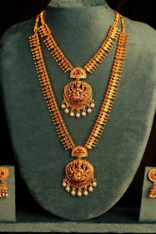 Gold necklace and earrings set on a green velvet stand against a black background