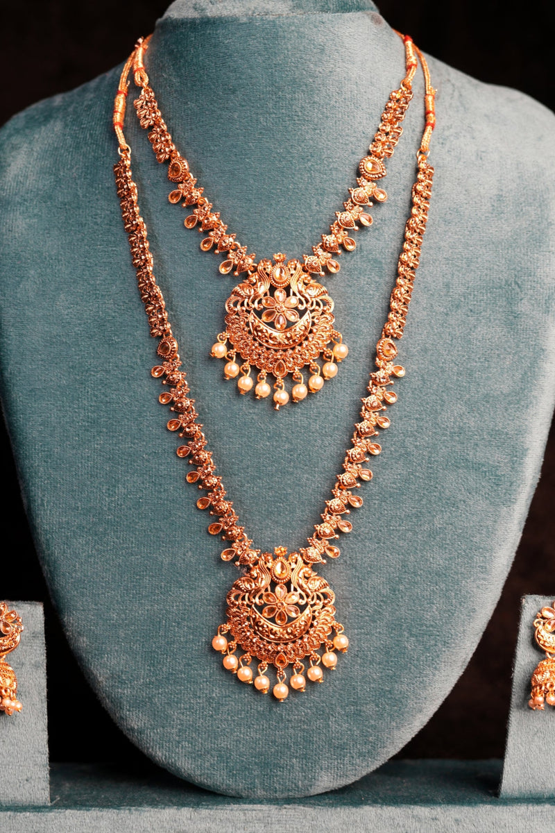 Rose gold necklace and earrings on a gray stand against a black background