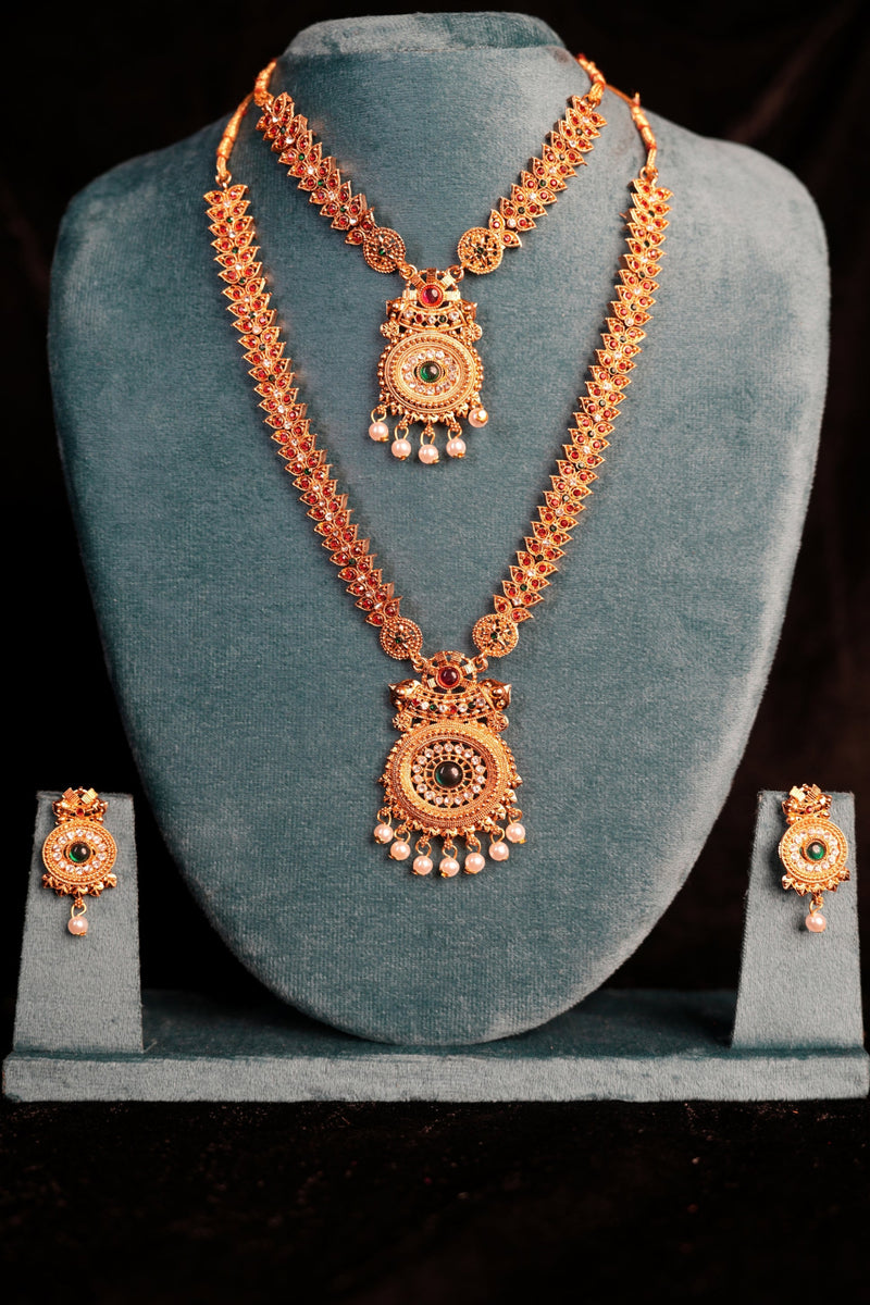 Ornate gold necklace and earrings set on a gray stand against a black background