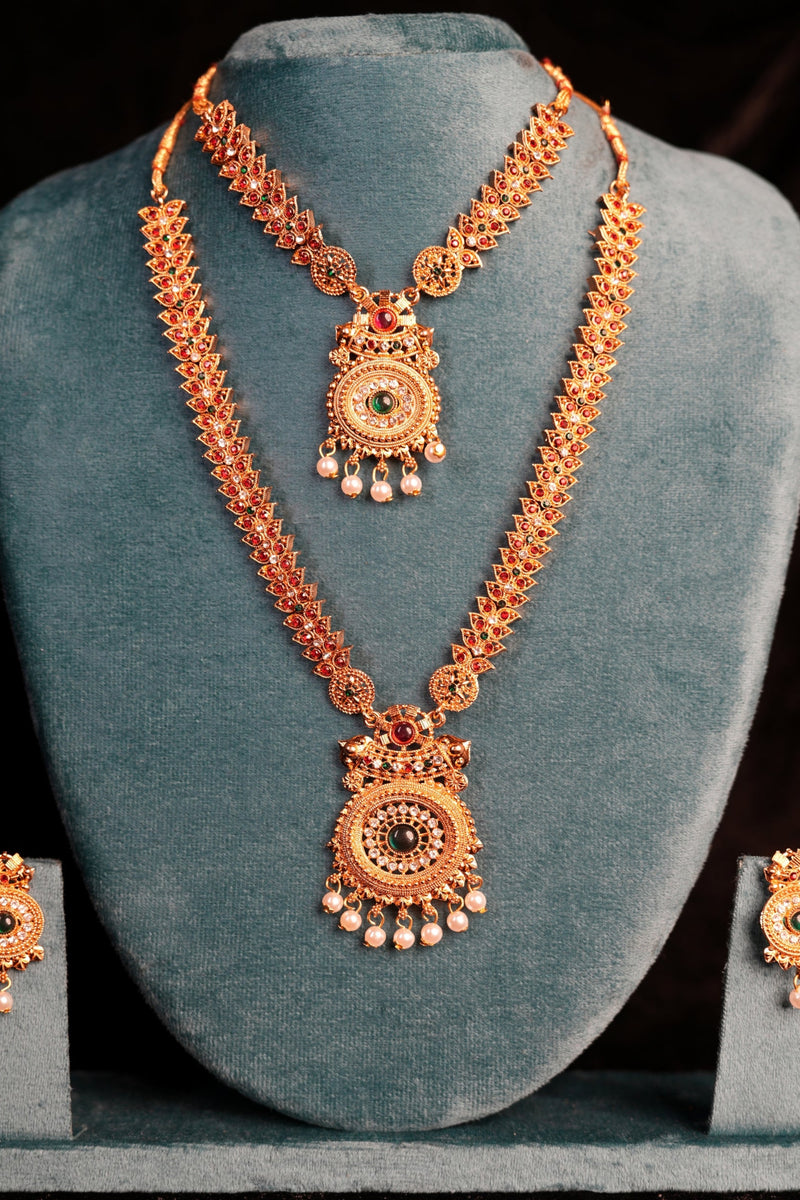 Ornate gold necklace and earrings set on a gray stand against a black background
