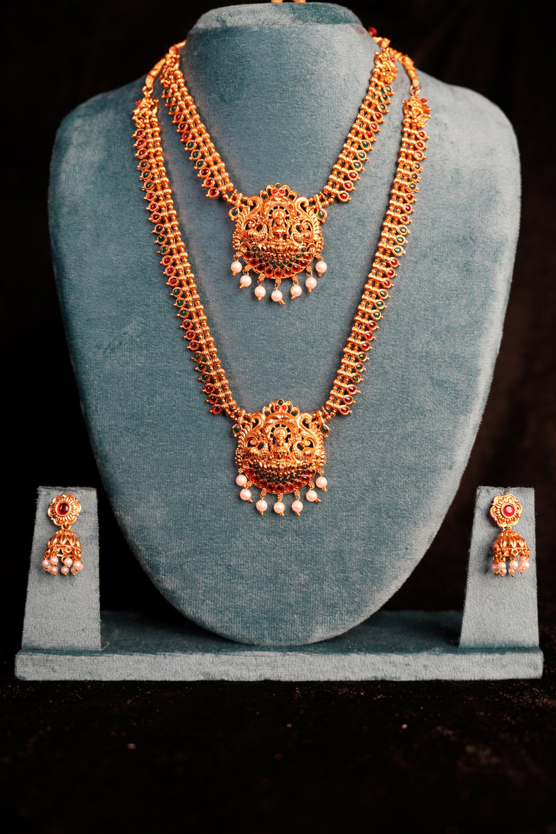 Ornate gold necklace and earrings on a teal cushion with a dark background