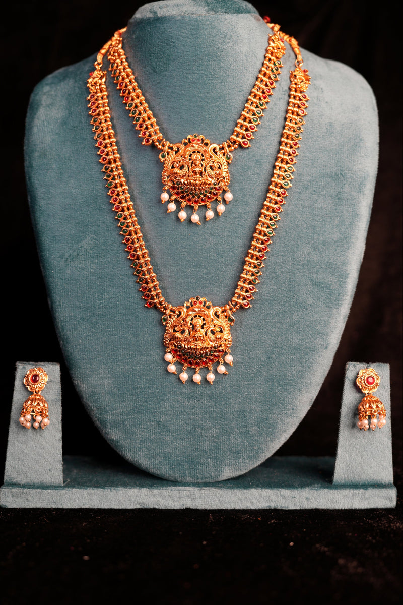 Ornate gold necklace and earrings on a gray stand against a black background