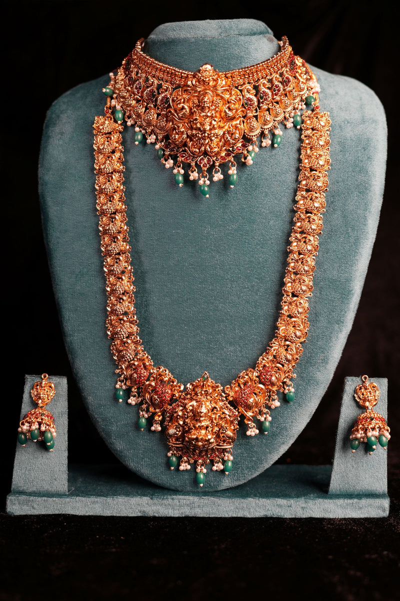 Ornate necklace and earrings set on a gray stand against a black background