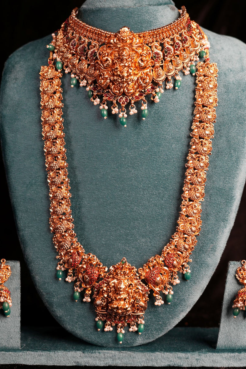 Ornate necklace and earrings set on a gray stand against a black background