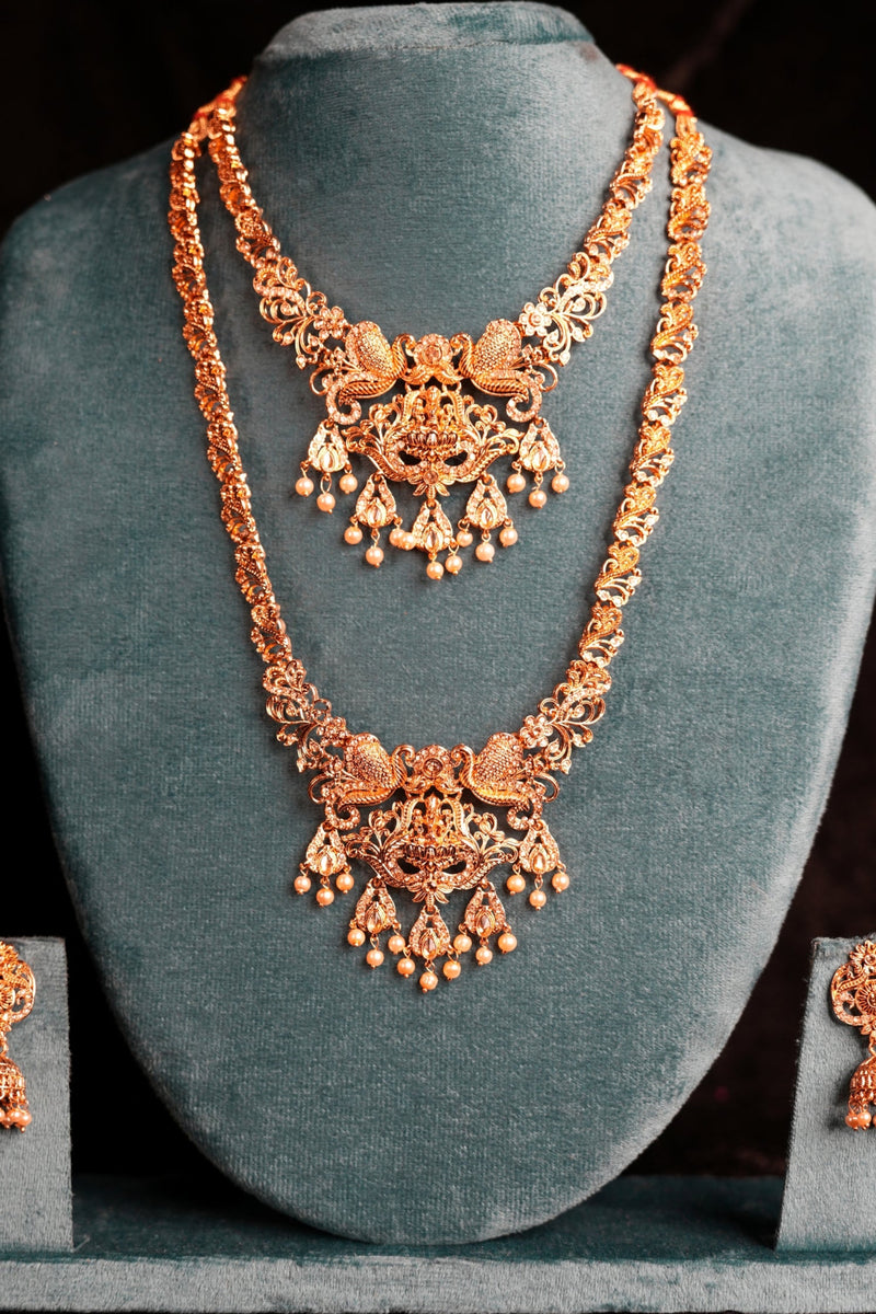Ornate gold necklace and earrings on a gray stand against a dark background