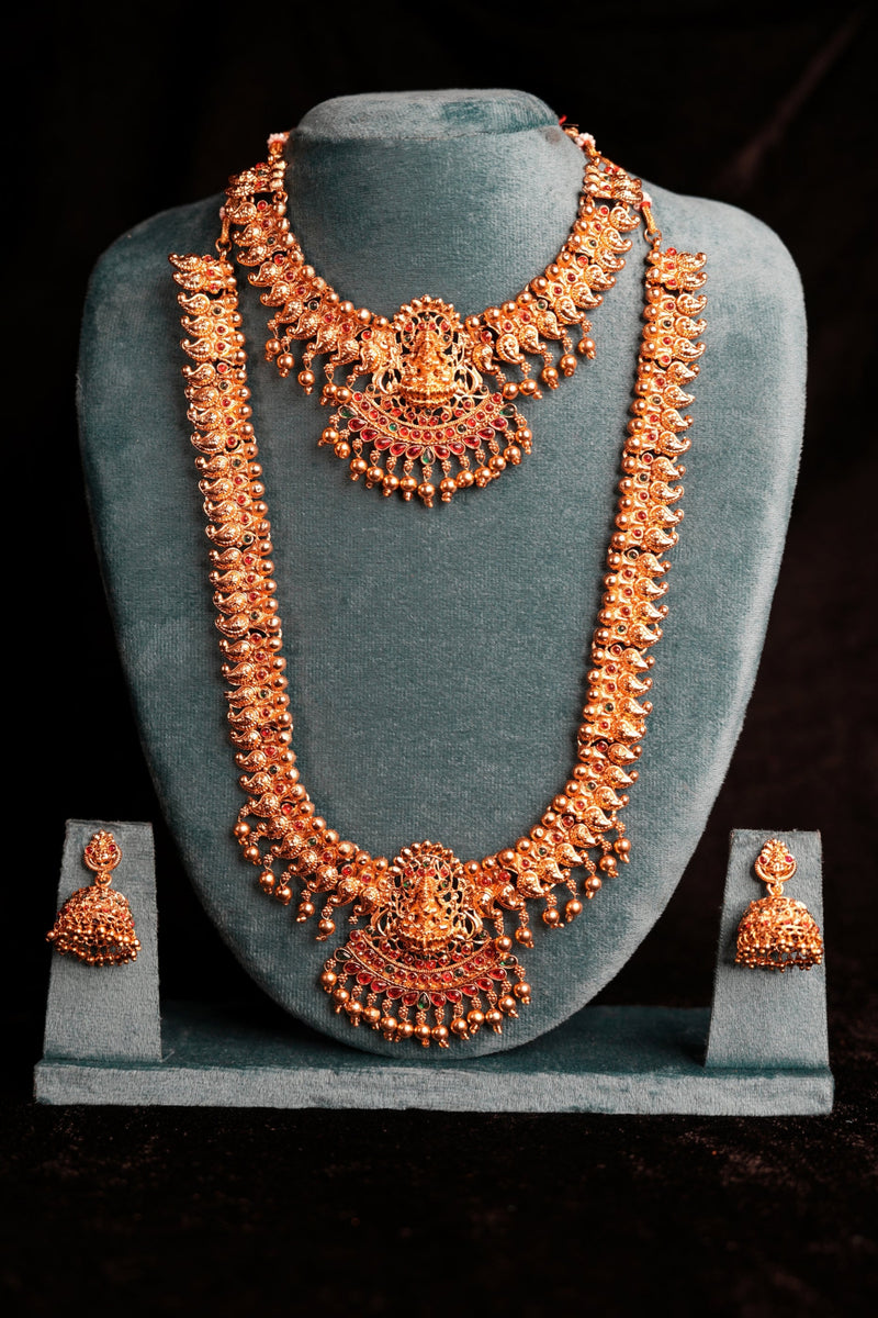 Ornate gold necklace and earrings set on a gray stand against a black background