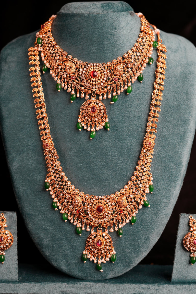 Ornate gold necklace with green beads on a gray cushion against a black background