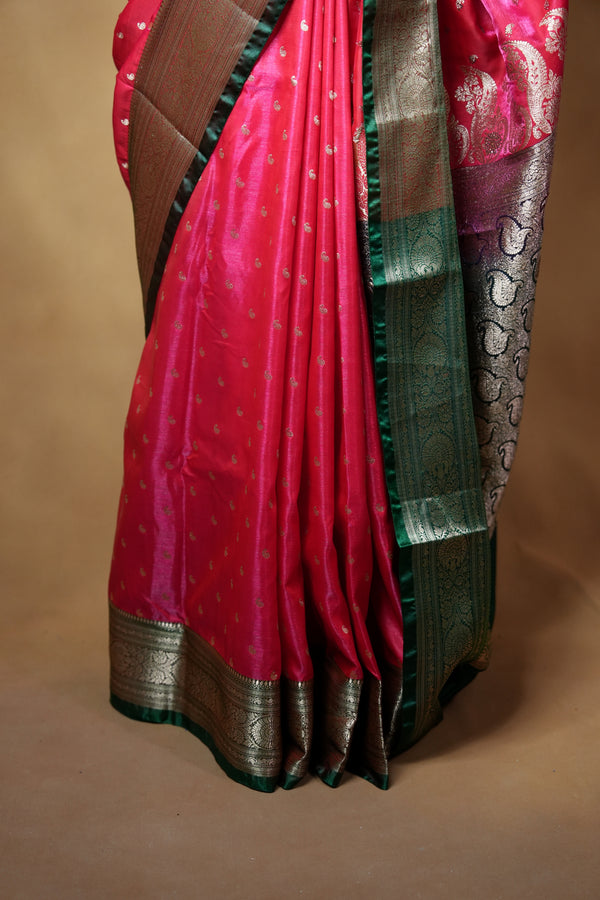 A folded red silk saree with a metallic gold border and a green pallu, displayed against a plain beige background.