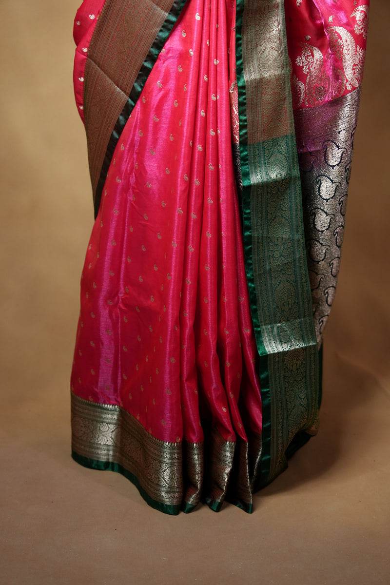 A folded red silk saree with a metallic gold border and a green pallu, displayed against a plain beige background.