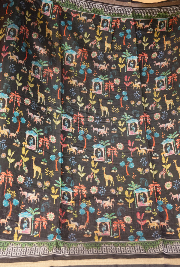 A black fabric, likely a saree or scarf, featuring a vibrant, multicolored all-over print of safari animals (giraffes, elephants, lions), palm trees, and architectural motifs, finished with a decorative border.