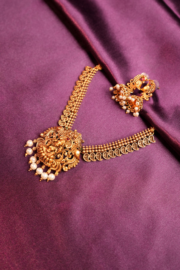An ornate gold-toned traditional Indian hair ornament (jhumka) with pearl embellishments, displayed on a draped purple satin fabric.