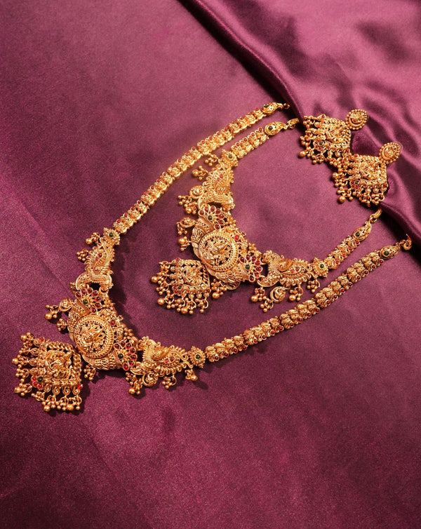 An ornate gold-toned traditional jewelry set with a necklace, earrings, and matching bracelet arranged on a rich magenta satin fabric background.