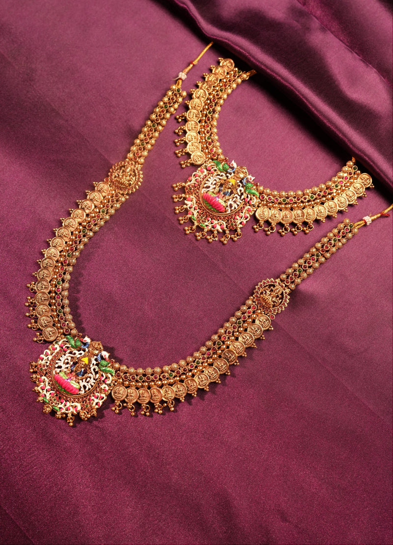 Gold-toned traditional Indian jewelry set featuring a necklace and matching choker with intricate filigree work and colorful enamel accents in pink, green, and red, displayed on a draped maroon satin fabric.