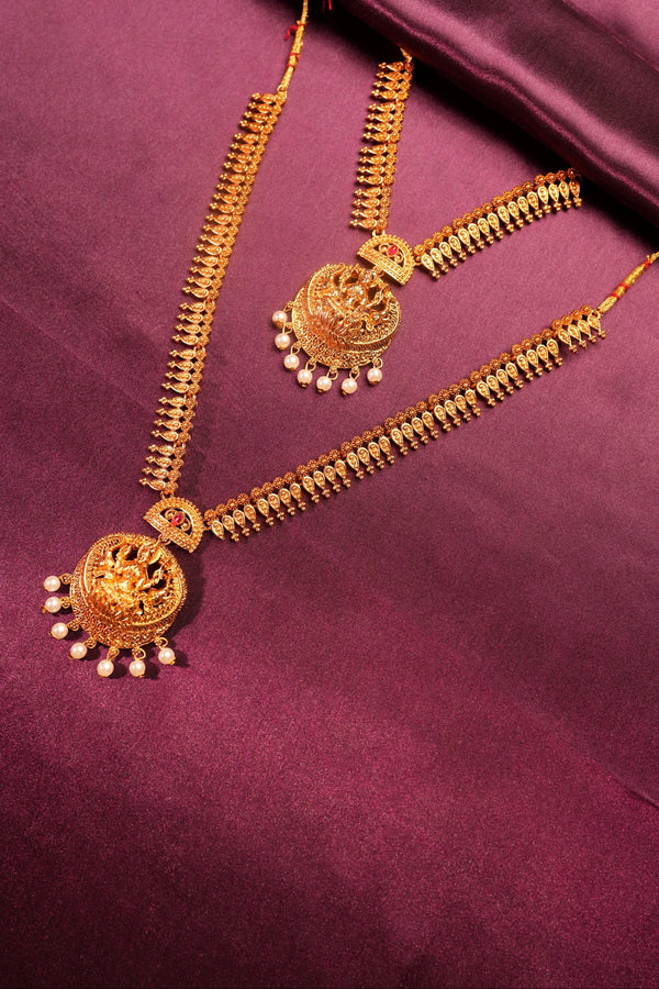 Gold-toned traditional jewelry set with ornate circular motifs, dangling chain elements, and small pearl-like accents, arranged on a rich purple satin fabric background.
