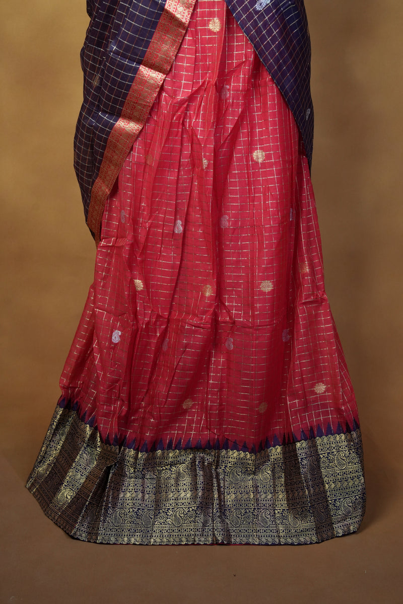 A folded red and navy blue saree with a metallic gold border and small gold motifs, displayed against a plain brown background.