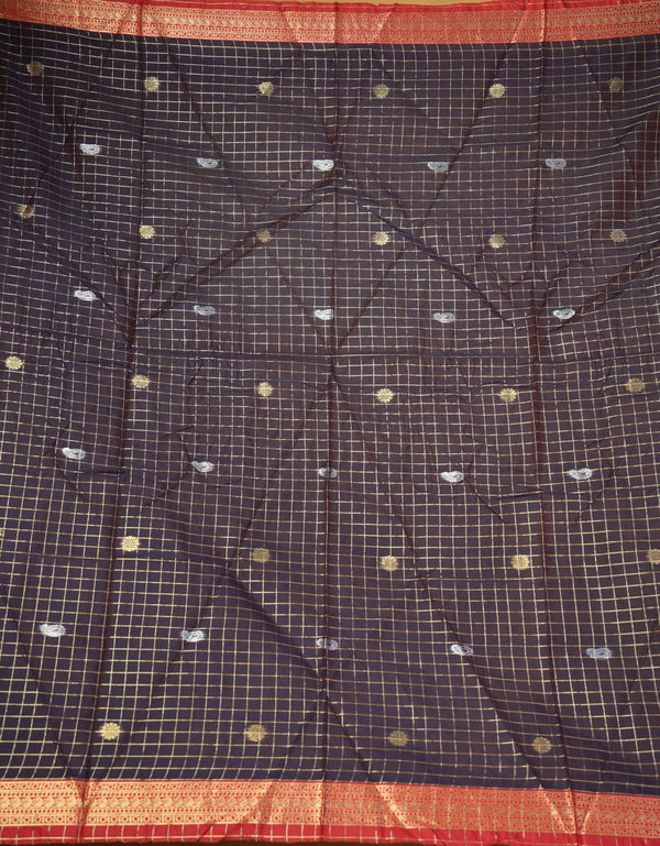 A close-up of a dark charcoal gray or black saree fabric with a fine gold grid pattern, decorated with small scattered gold and silver motifs, and finished with a wide red and gold border.