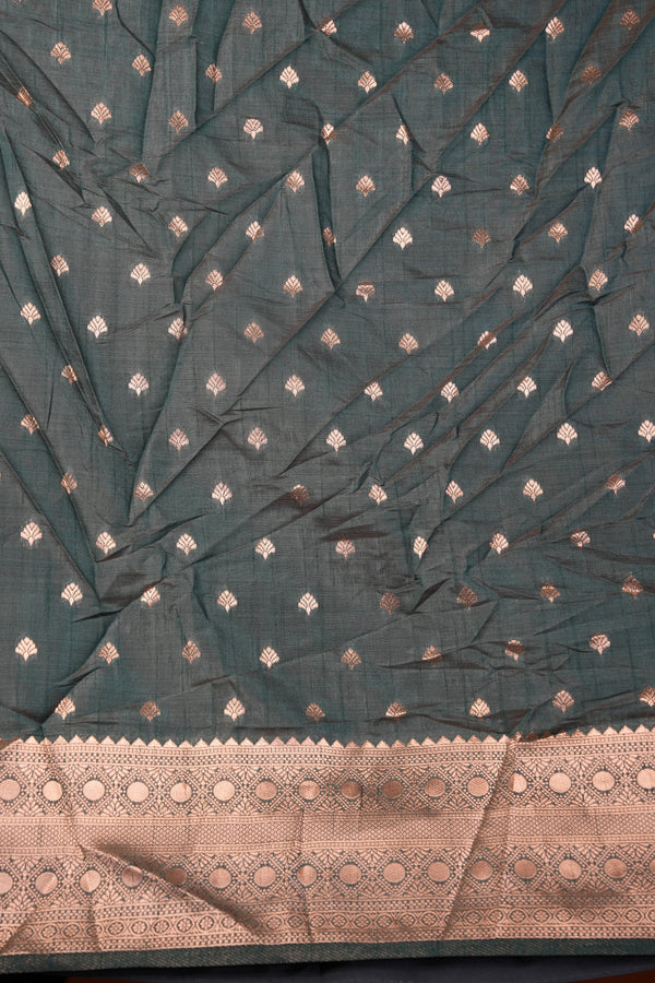 A dark teal-green saree fabric with small metallic gold and silver diamond motifs, featuring a wide beige border with intricate gold and silver embroidery.