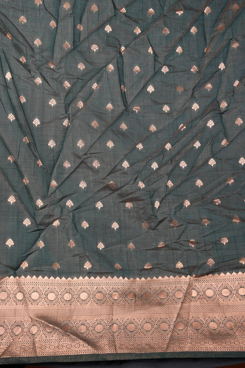 A dark teal-green saree fabric with small metallic gold and silver diamond motifs, featuring a wide beige border with intricate gold and silver embroidery.