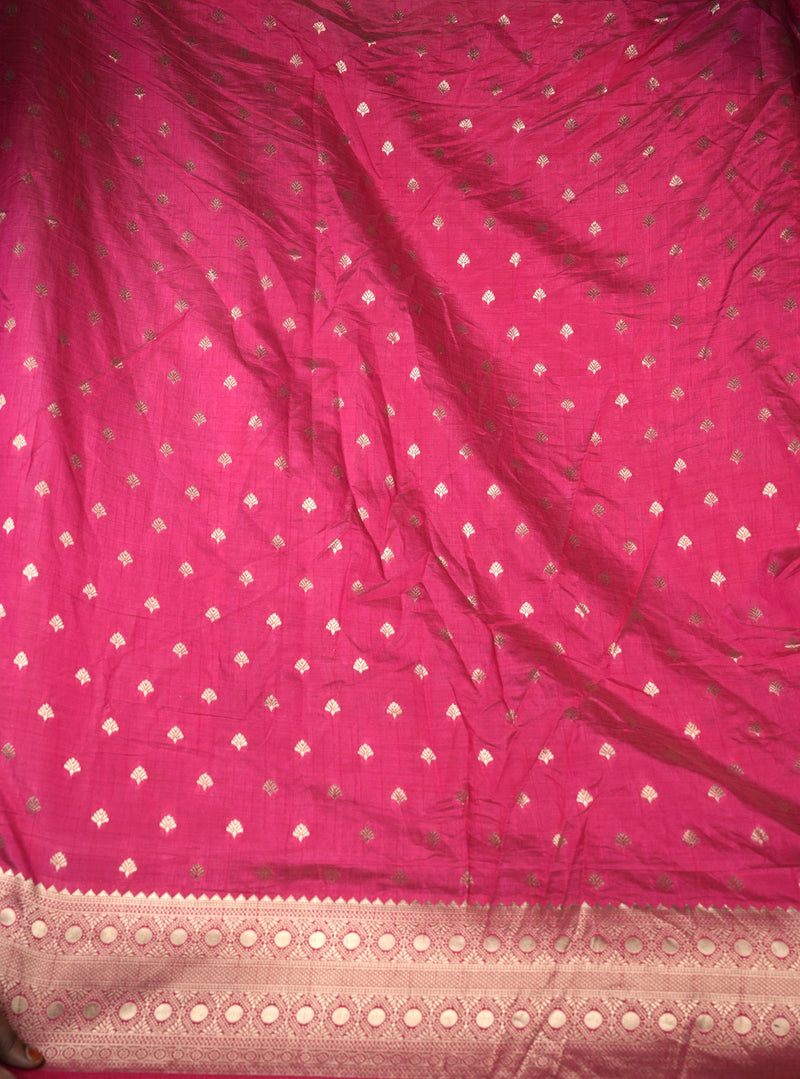 A close-up of a bright pink fabric, likely a saree, featuring a repeating pattern of small metallic gold diamond motifs and a decorative gold border along the bottom edge.