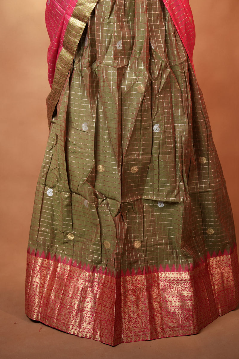 A close-up of a draped fabric garment, likely a sari or scarf, with a metallic olive-green body, small gold motifs, and a wide red border.
