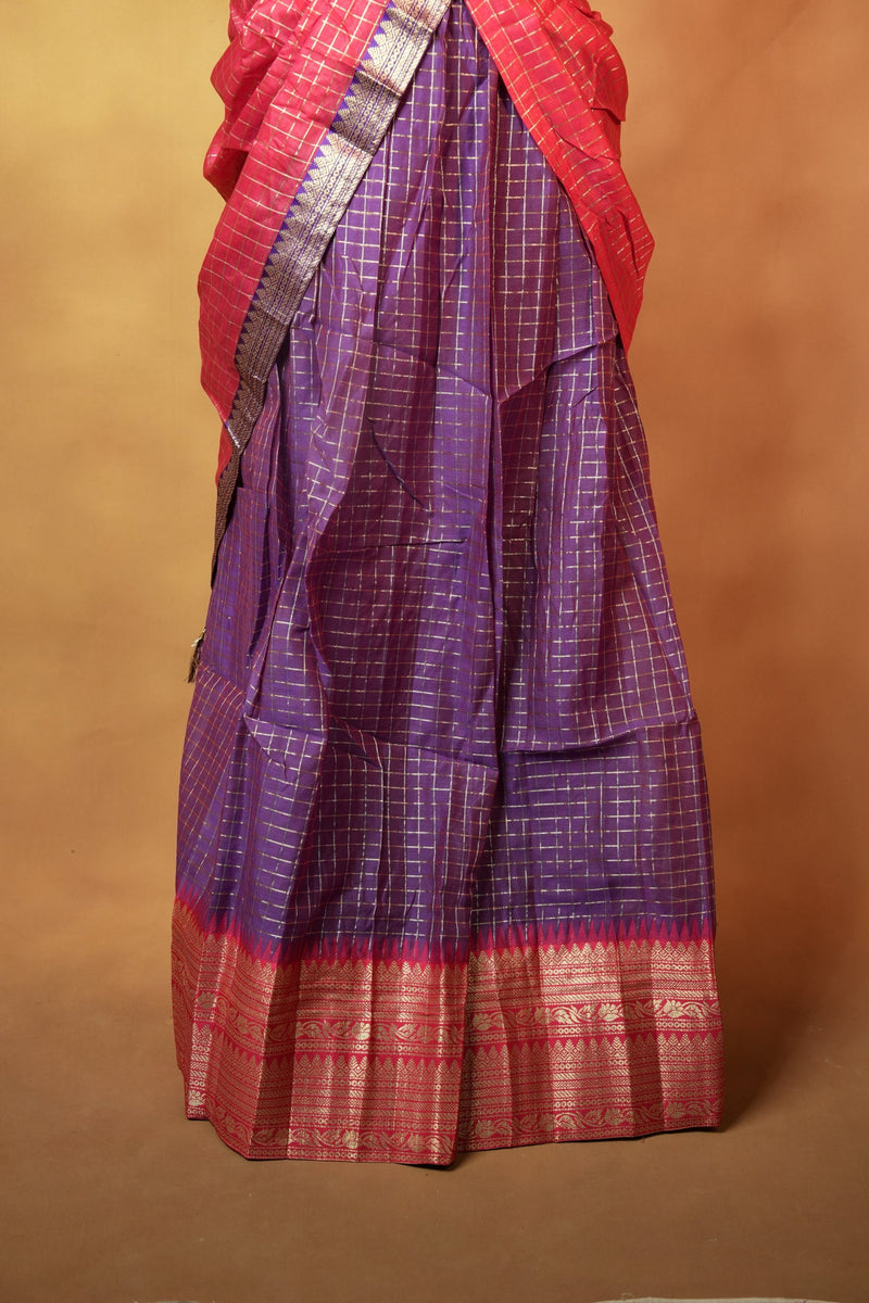 A folded purple and red saree with a metallic silver border, displayed against a plain brown background.