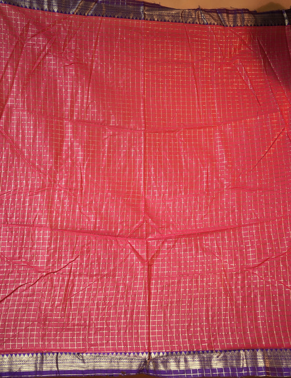 A close-up of a red fabric, likely a saree, featuring a fine white grid pattern and a purple and gold border at the bottom.
